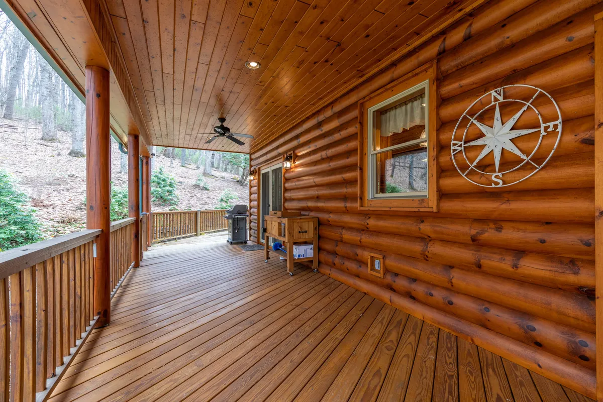 A tranquil wooden deck adjacent to the log cabin offers outdoor dining space, a grill, and comfortable seating. The compass decoration and ambient lighting suggest a place for group meals, conversation, and soaking in the natural surroundings.