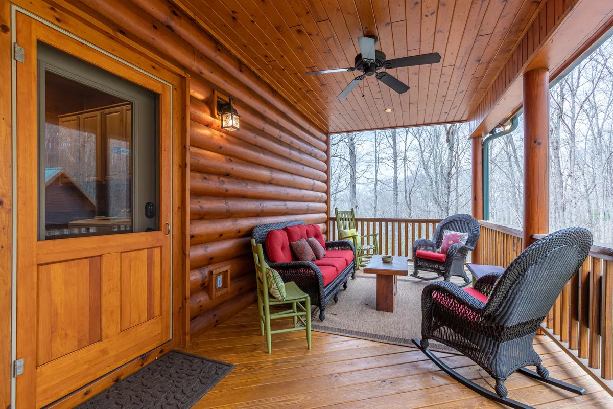 This exterior shot highlights the rustic wooden log walls of The Forge and features comfortable outdoor seating and a coffee table, with large windows framing the natural surroundings. The porch area is spacious and inviting, suggesting a seamless transition between indoor comfort and outdoor enjoyment.