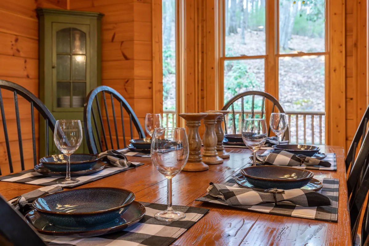 A spacious dining area set for a festive meal, showcasing a large wooden table with plated dishes, wine glasses, and a rustic cabinet. The setting radiates warmth and is ideal for family gatherings, holiday feasts, or friends sharing stories after an adventure-filled day.