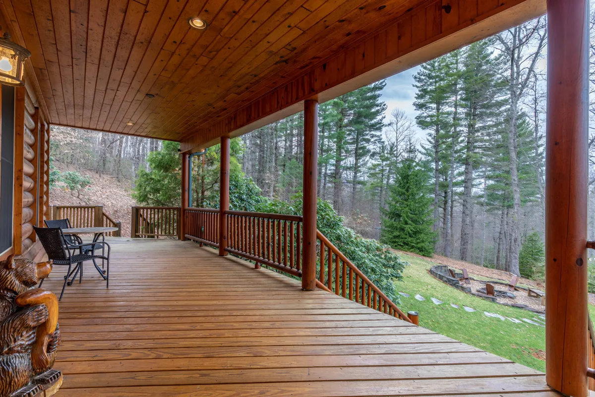A wooden deck with sturdy log siding, surrounded by mature trees. Outdoor seating overlooks the natural landscape, offering a tranquil spot to unwind. The scene hints at all-season use—imagine snowy vistas in winter or lush greenery in summer.