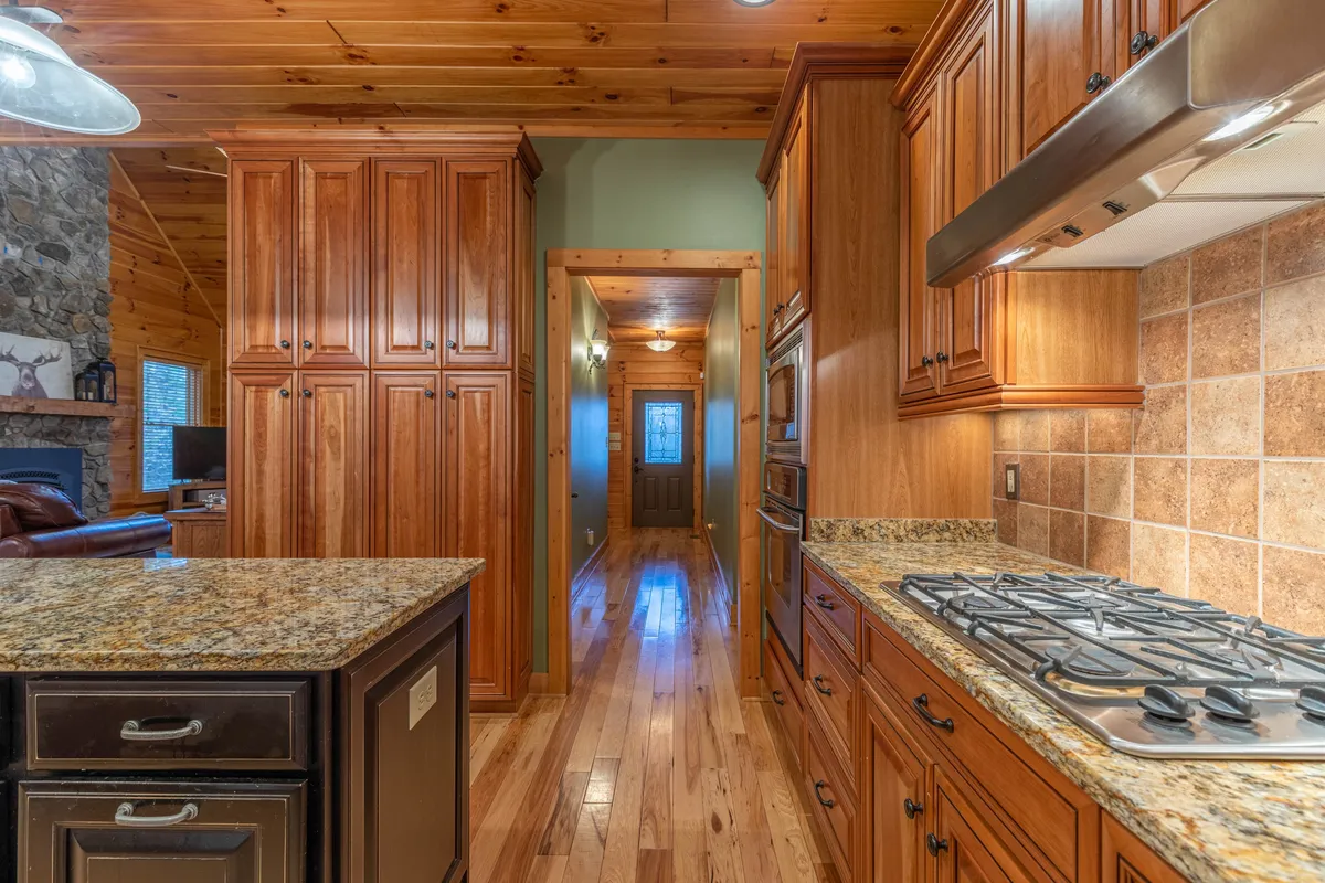The photo centers on a cozy, well-appointed kitchen with a granite countertop, warm wood cabinetry, stainless steel appliances, and a rustic stone wall. The space exudes a welcoming, chef-inspired atmosphere perfect for family gatherings and culinary adventures.