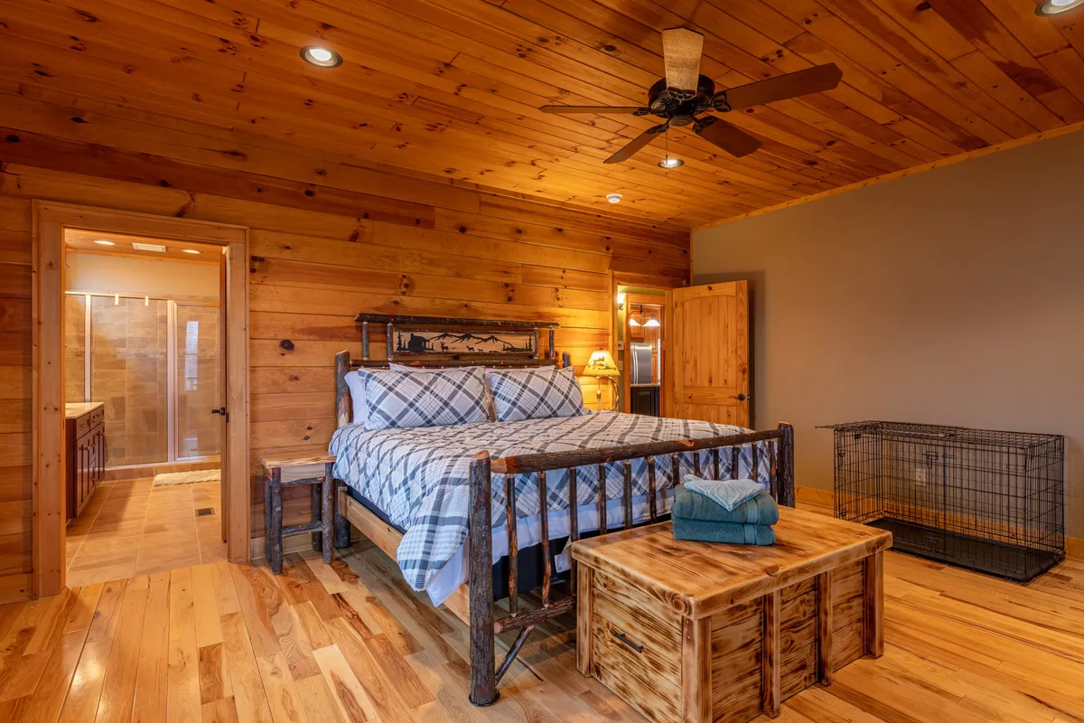 This image displays a warmly lit bedroom featuring a wooden bed frame with plaid bedding, a wooden ceiling, and a nightstand with a lamp. The environment exudes comfort and quiet, suitable for adults seeking a tranquil escape.