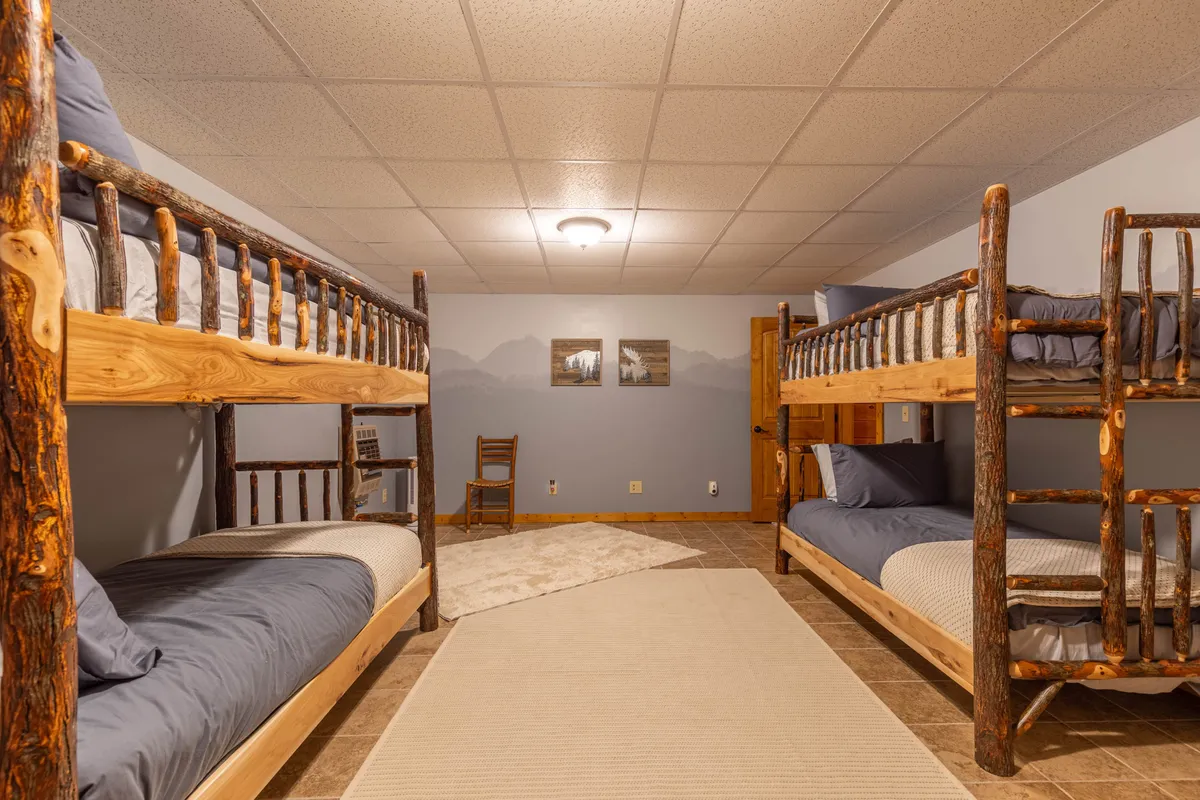 This image presents another view of a bunk room, including wooden bunk beds, friendly artwork on the wall, and additional cozy touches. The mood is relaxed and welcoming, hinting at memorable sleepovers and shared moments.