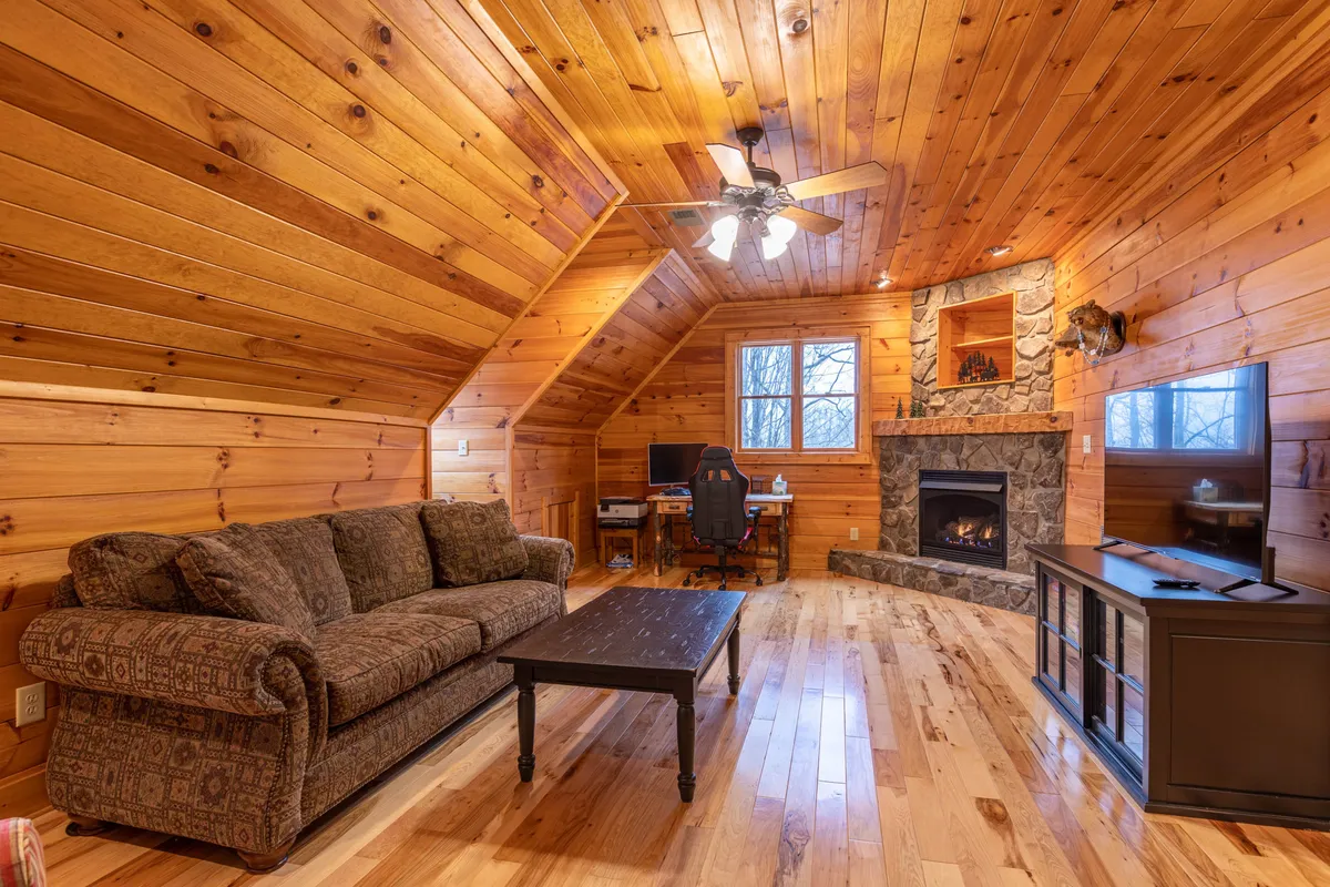 A warm, inviting living room with a prominent fireplace, wooden ceiling, comfortable sofa, and a coffee table arranged for relaxing after a day outdoors. The television and soft lighting contribute to a cozy atmosphere, suggesting a great spot to unwind during colder months.
