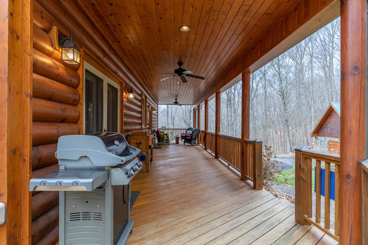 A cozy exterior deck with comfortable rocking chairs and a grill, framed by the classic log walls and railings of the cabin. The scene suggests both morning relaxation and evening barbecues, with ample space for adults and children to gather, eat, and socialize amid natural surroundings.