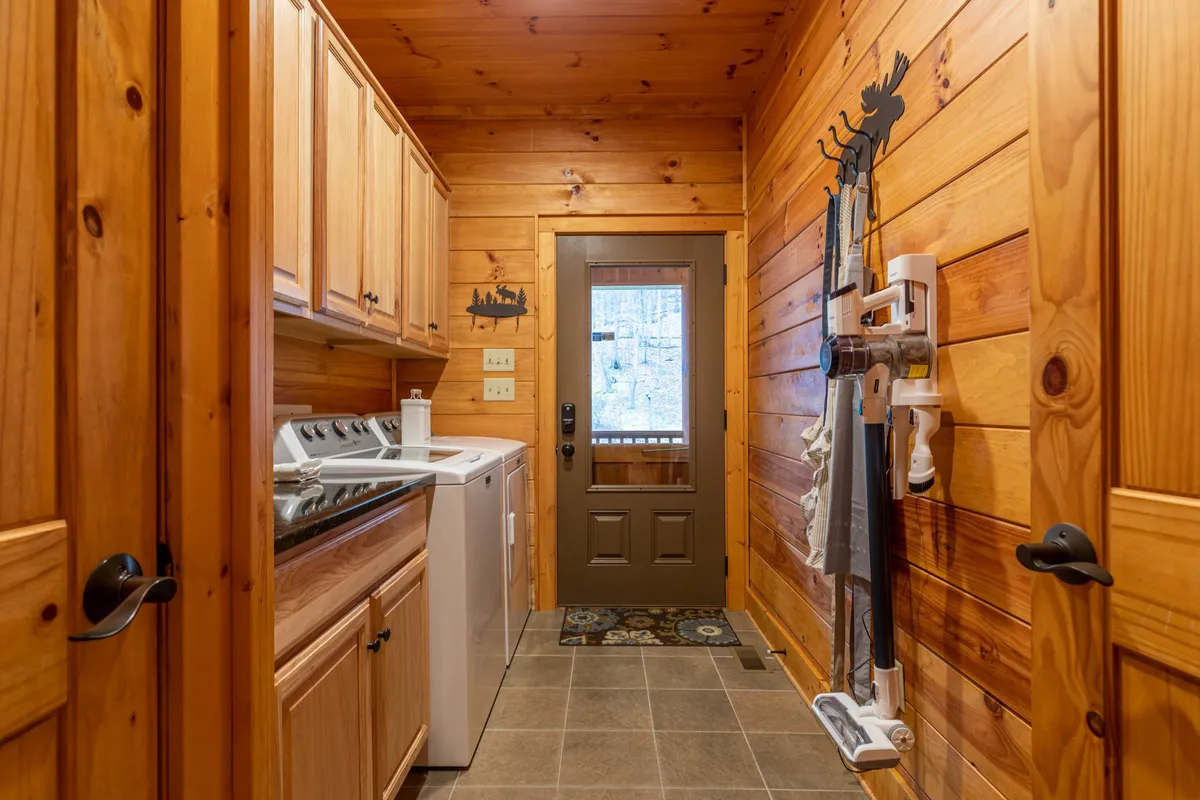 A mudroom or entryway featuring a washer and dryer, wooden cabinets for storage, a back door entry, and a decorative moose silhouette. The space is practical and tidy, offering a welcoming feel for those entering the home, and easy access for managing gear after outdoor adventures.