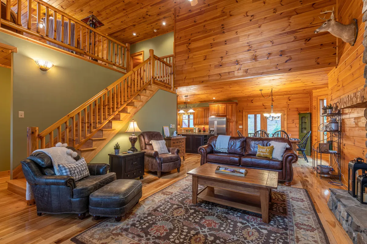 A cozy living area featuring a wooden staircase, a plush leather sofa, coffee table, a fireplace, and a decorative rug. The inviting atmosphere is ideal for relaxing after a day of adventure, with enough space for group gatherings and pets to curl up after outdoor outings.