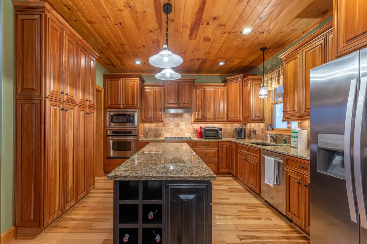 A spacious open-concept kitchen with granite countertops, wooden cabinetry, and a central island featuring wine storage. The kitchen is bright and welcoming, with stainless steel appliances and ample space for preparing meals together.