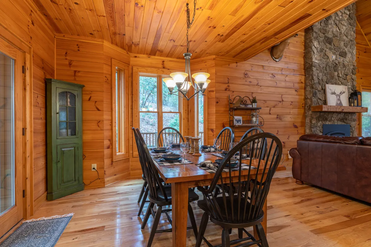 A warm dining area highlighted by a large wooden table, elegant chandelier, wooden cabinets, and a comforting stone fireplace. The space is set up for intimate gatherings and cozy evenings.